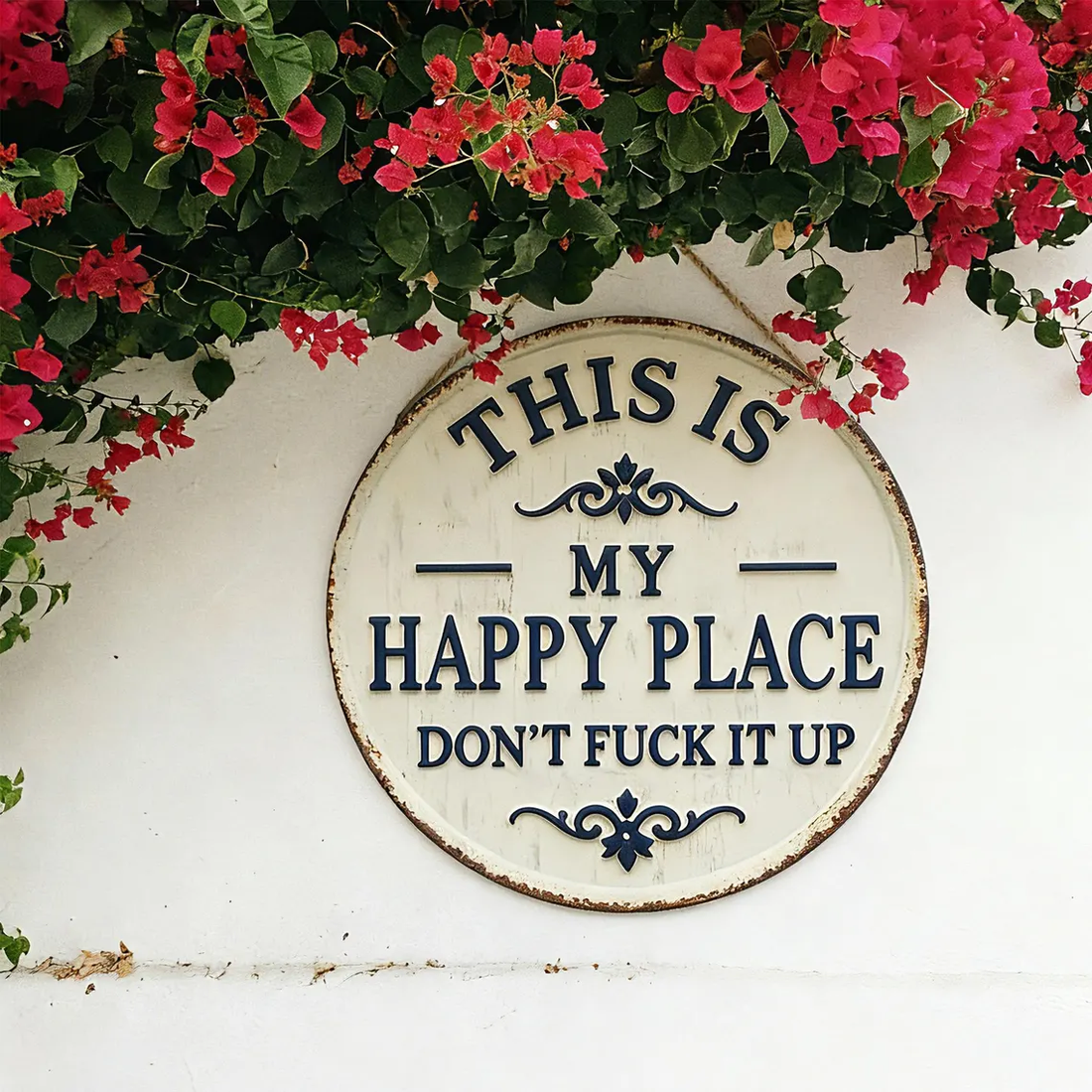 Vintage round tin sign reading 'This is my happy place' on white wall with pink flowers above.