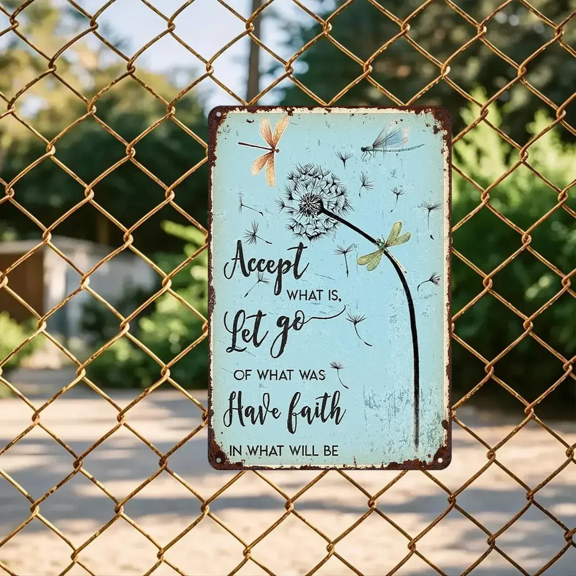 Vintage tin sign with dandelion, dragonflies, and inspirational quote on a fence outdoors.