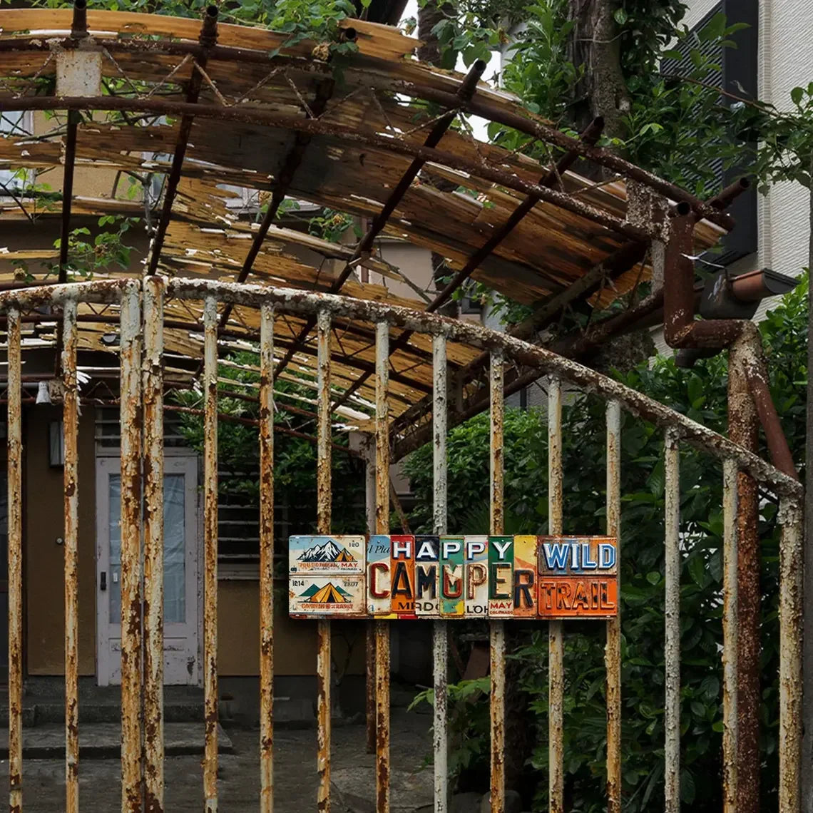 Rustic metal gate with colorful vintage tin sign reading 'Happy Camper Wild Trail'