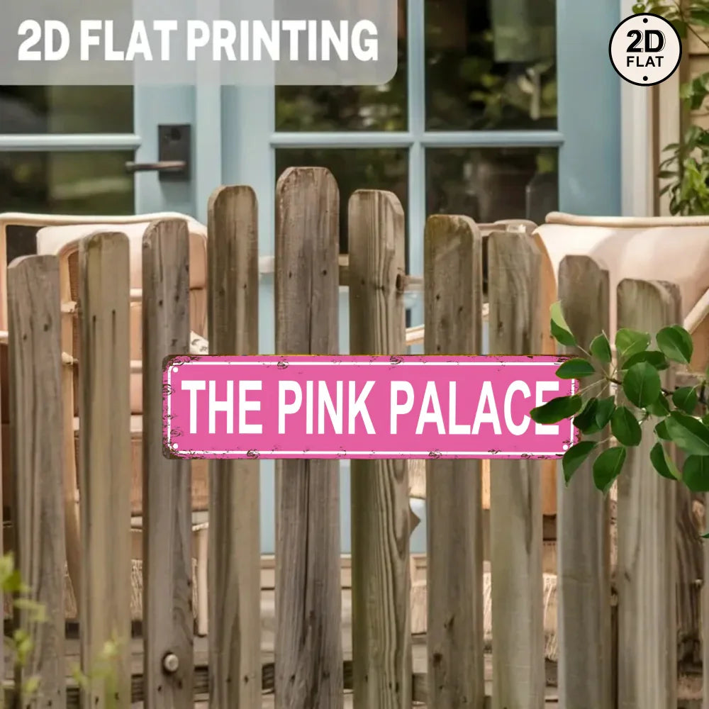 Vintage pink metal sign reading 'The Pink Palace' on a rustic wooden fence outdoors